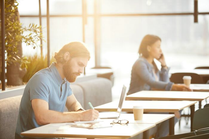Man focused on writing at a cafe table with a laptop, illustrating karma stories in a calm, bright coworking space.