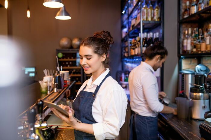 A smiling barista uses a tablet, while a male coworker prepares drinks in the background. Many people rage quit their jobs.