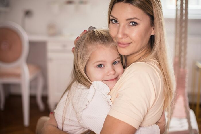 A smiling mother embraces her young daughter, both looking at the camera. Advice for dads raising daughters.