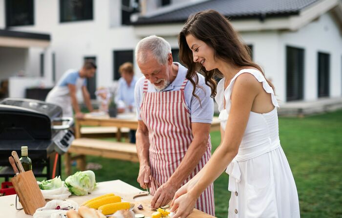 A dad in an apron and his daughter smiling while preparing vegetables for a barbecue. Women giving dads advice on raising daughters.