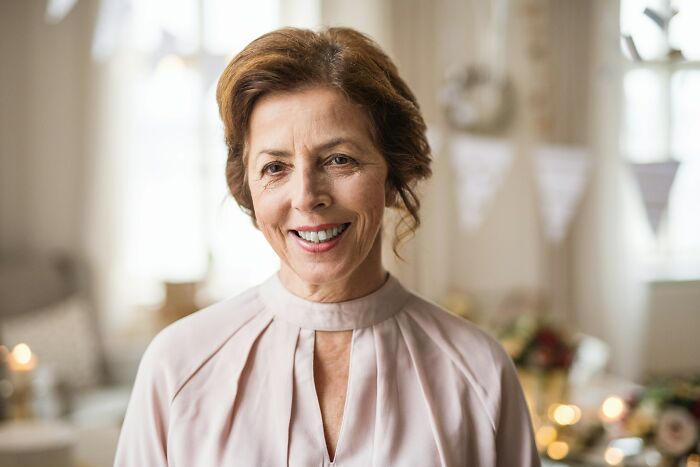 Mature woman smiling warmly in a softly lit indoor setting, capturing moments from wild bachelor and bachelorette parties.