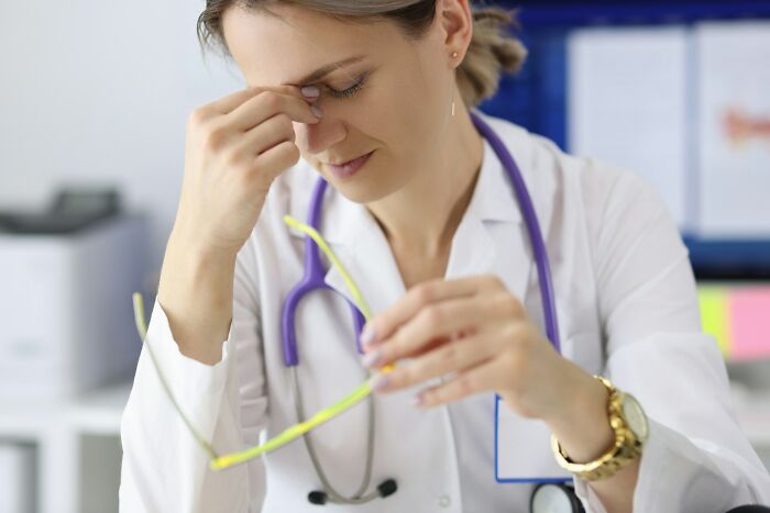 Stressed female employee in white coat holding glasses, experiencing burnout, reflecting wild times quitting job immediately.