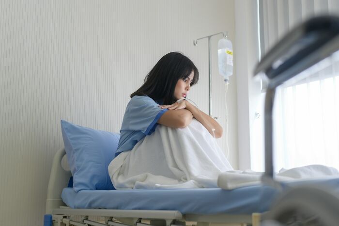 Young woman looking thoughtful and isolated in hospital bed, reflecting on wild bachelor and bachelorette party experiences.