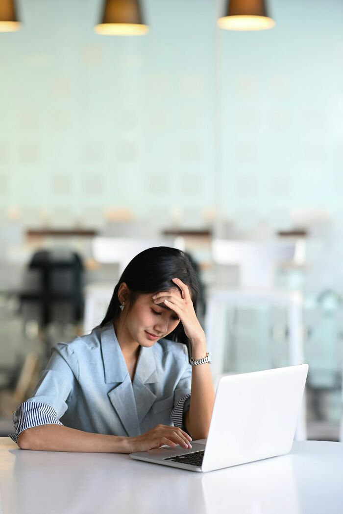 A stressed woman at a laptop, head in hand, contemplating whether to rage quit her job.