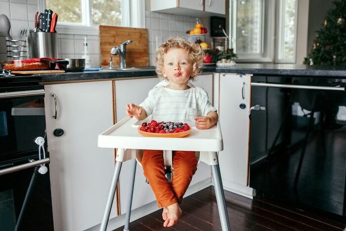 Toddler sitting in a high chair eating berries in a kitchen, illustrating tips and tricks parents just had to share.