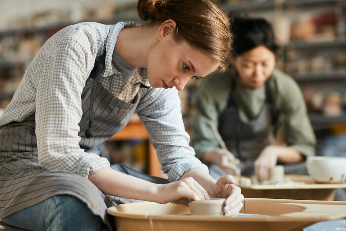 Young woman focused on pottery wheel creating clay art, illustrating themes of weaponized incompetence in creative work.