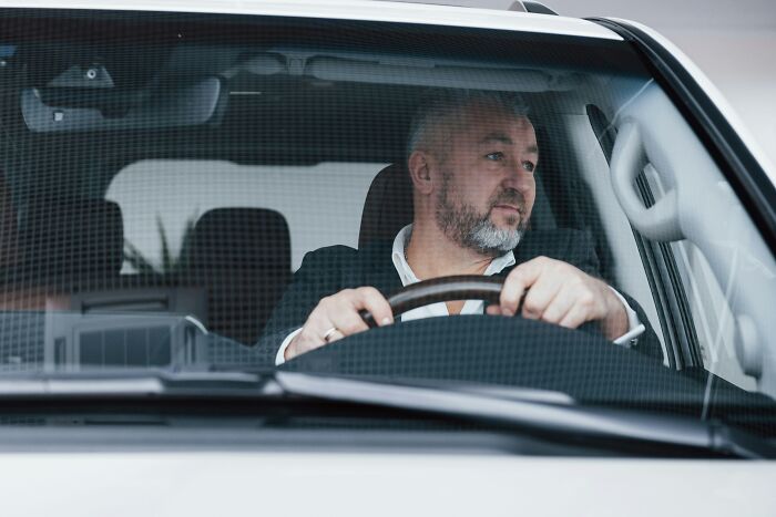 A bearded man in a suit drives a car, looking out the front windshield. This image relates to juicy and messy anonymous confessions.