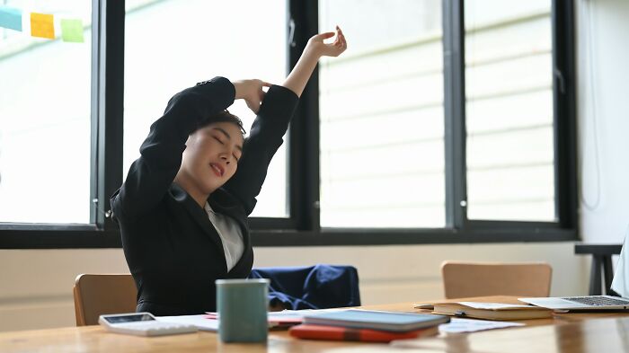 Young woman stretching at desk in bright office, illustrating how random life decisions can lead people to the right place.