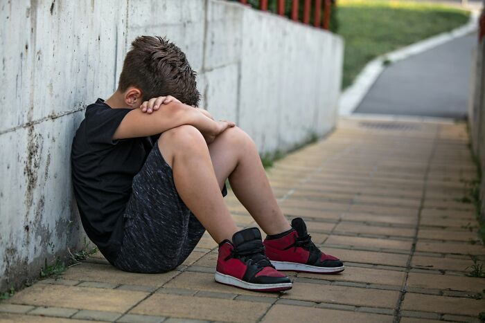 Boy sitting alone on pavement with head down, depicting the emotional impact of horrible bullies on life.