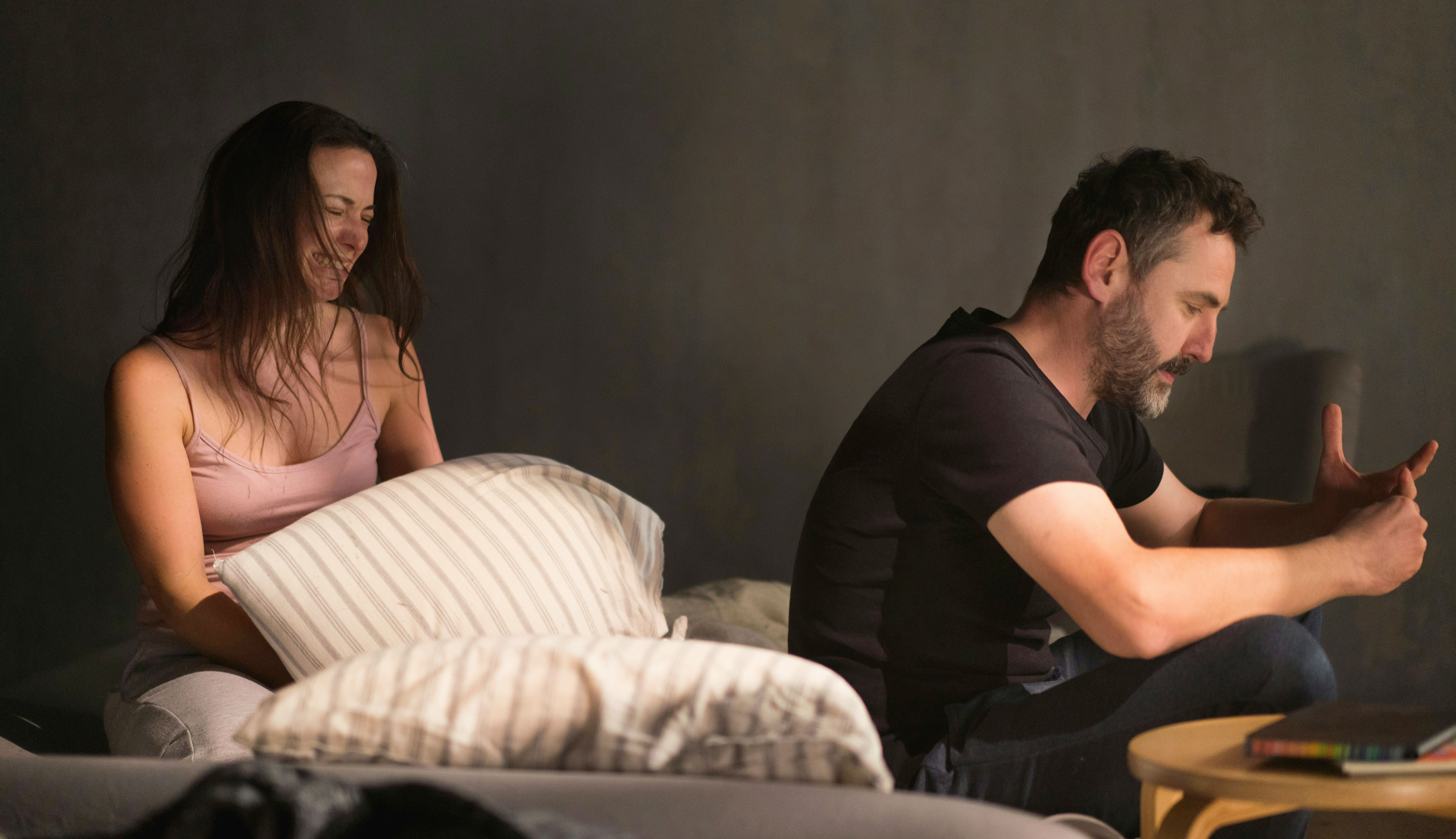 Woman and man, both looking upset, sitting on a bed in a dimly lit room, facing away from each other, considering divorce.