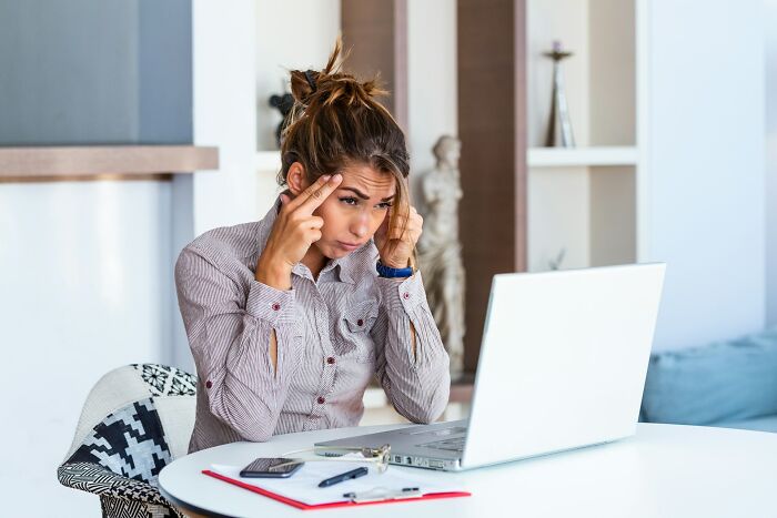 Young woman looking stressed while using laptop, experiencing embarrassment after sending accidental message online.