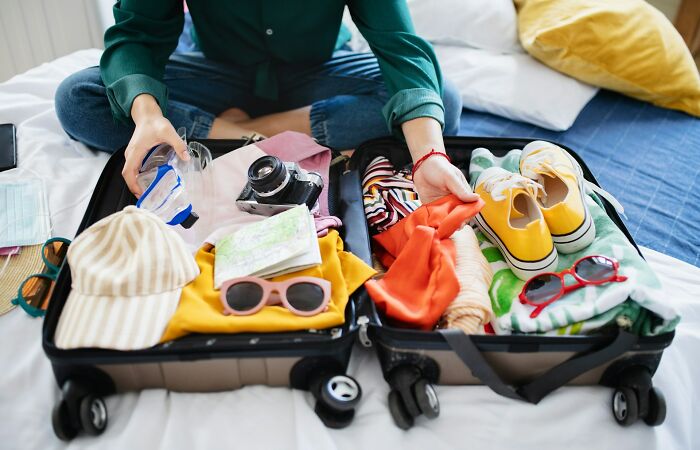 Person packing a suitcase with clothing, shoes, and travel items illustrating tips and tricks parents share for trips and travel.