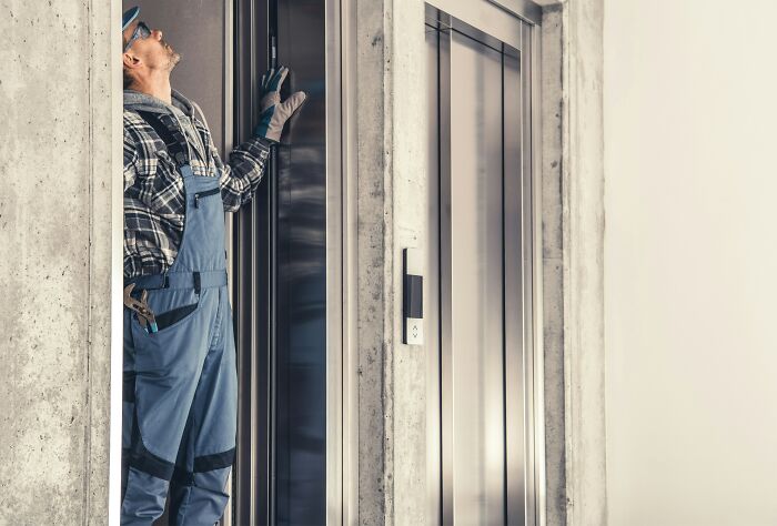 Elevator mechanic in blue overalls inspecting elevator doors in a modern building, focusing on elevator pits maintenance.