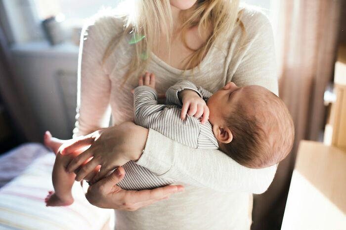 A woman cradles a sleeping baby, representing the challenges and joys of family, especially with a MIL.
