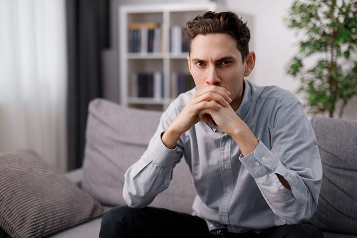 Young man feeling like a science experiment at home, looking thoughtful and concerned while sitting on a couch.
