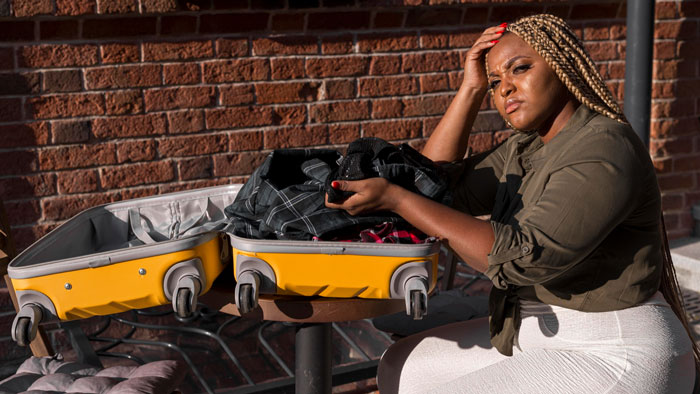 A distraught woman clutches her head beside a suitcase filled with clothes. Her husband's affair caused this emotional distress.