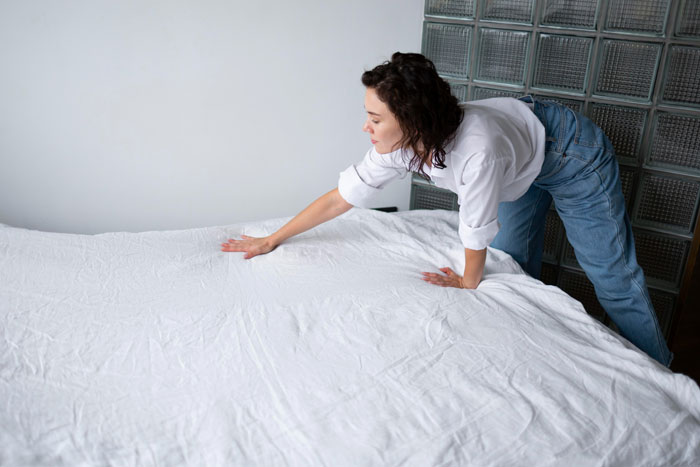 Woman making bed with white sheets in minimalist room