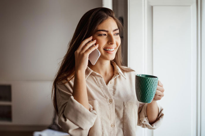 Smiling woman talking on phone while holding a cup
