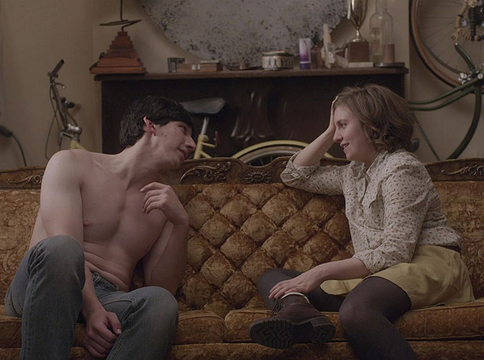 Adam Driver shirtless and Lena Dunham seated on a vintage couch in a casual scene from Girls set conversation.