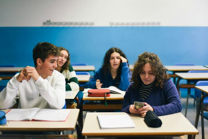 Students displaying intelligence in a classroom, engaging with each other while using phones and notebooks in a learning environment.