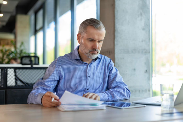 Middle-aged man in blue shirt reviewing documents at a desk, representing bankruptcy and financial penalties.