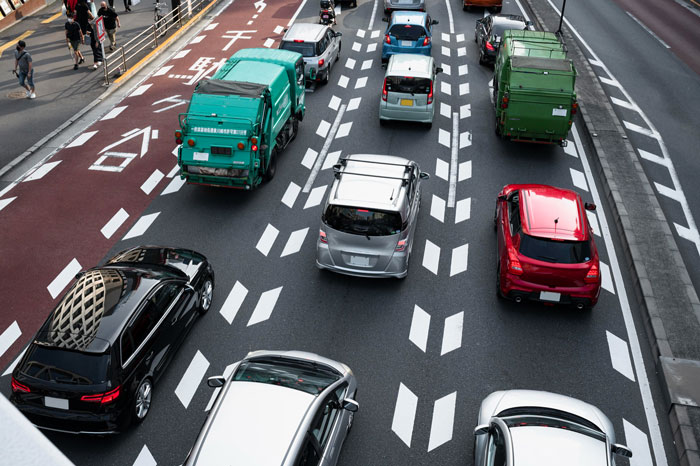 Overhead view of a multi-lane city street with various cars, trucks, and a driver in traffic.