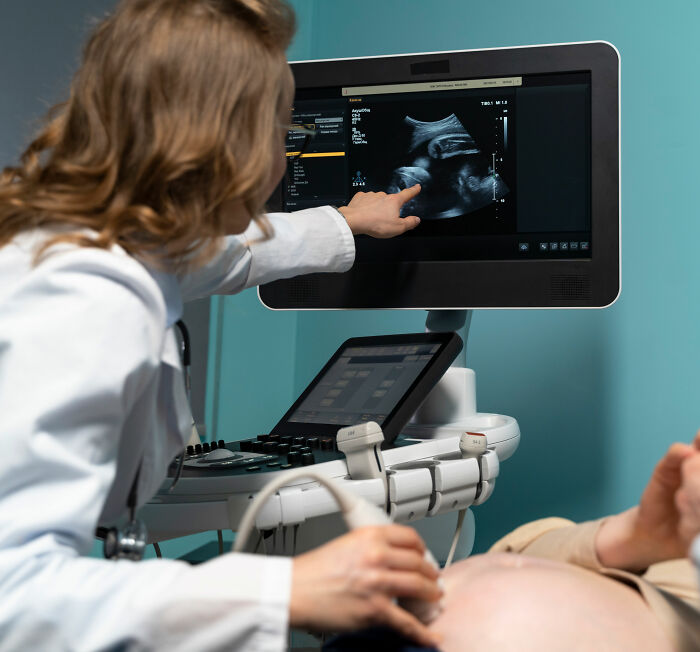 Pregnant doctor performing ultrasound, pointing at baby on screen showing baby peeing inside the womb in viral video.