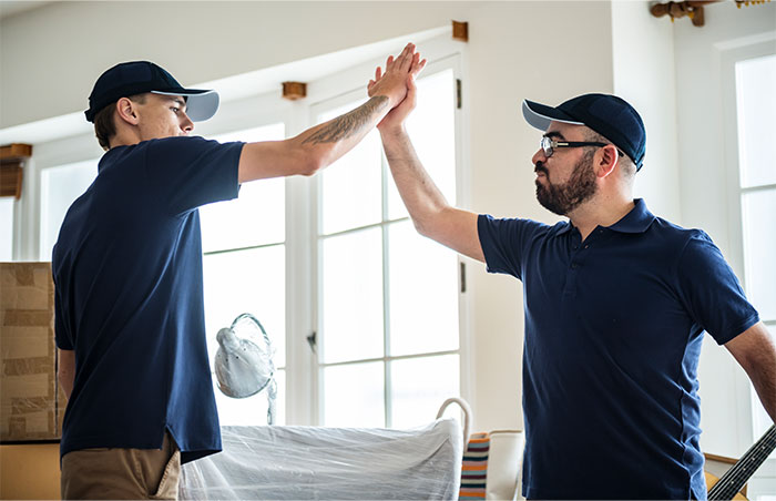 Two men in navy blue shirts and caps giving a high five showing support for an overworked and underpaid friend.
