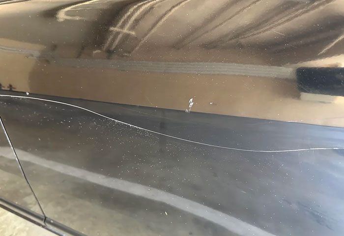 Close-up of a scratched black car door illustrating harmless but effective revenge on jerks with subtle damage.