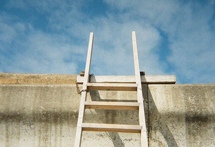 Wooden ladder leaning against a concrete wall under a partly cloudy sky, symbolizing harmless but effective revenge on jerks.