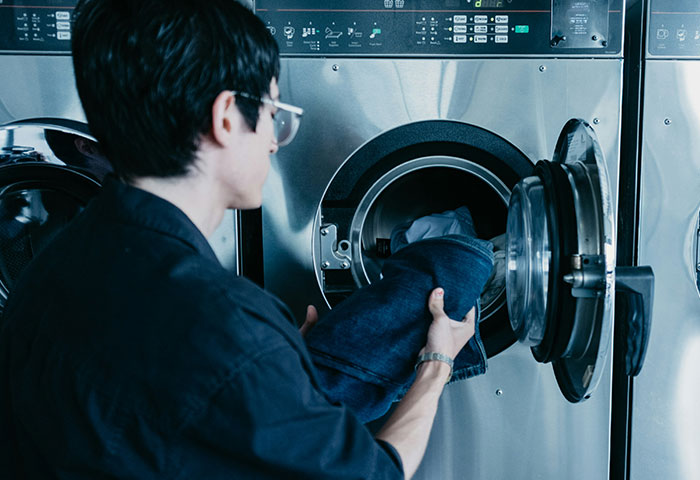 Person loading clothes into washing machine showcasing harmless but effective ways people got revenge on jerks.