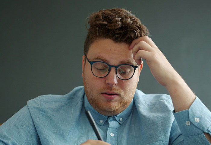 Man in glasses and blue shirt looking focused while planning harmless but effective revenge on jerks ideas.