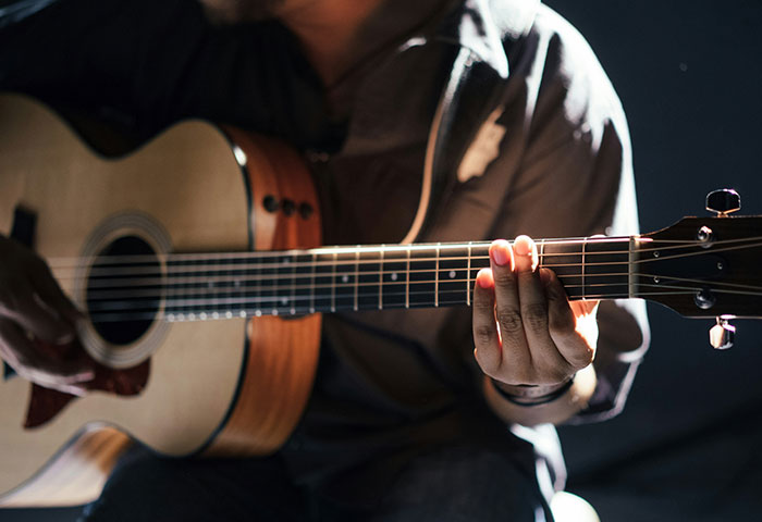 Person playing acoustic guitar in low light, illustrating harmless but effective ways people got revenge on jerks.