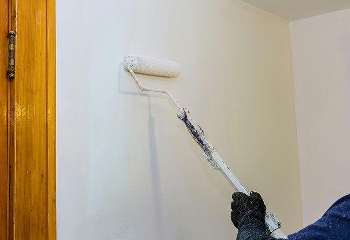 Person wearing black gloves using a paint roller to cover a wall as a harmless but effective way to get revenge on jerks