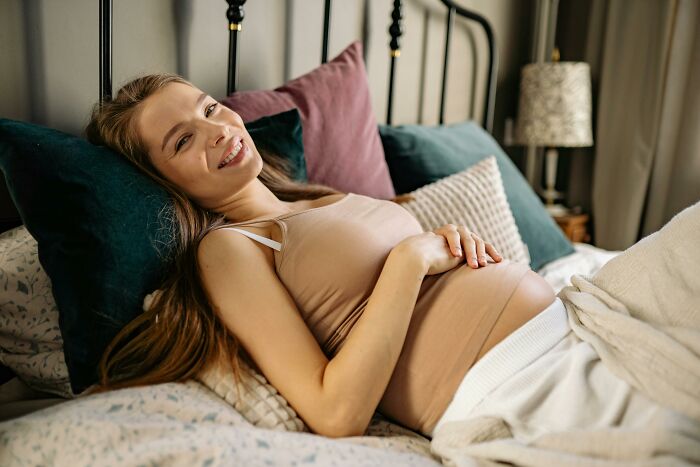 Pregnant woman reclining on bed with pillows, smiling comfortably in a calm healthcare setting at home.