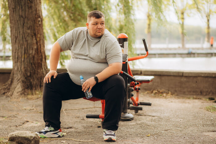 Man in casual clothes resting on outdoor gym equipment holding a water bottle, reflecting healthcare workers advice.