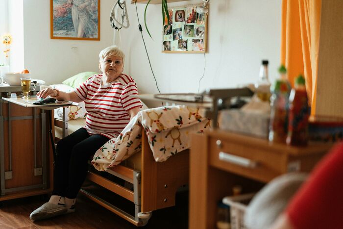 Elderly woman sitting on a hospital bed in a healthcare setting, highlighting healthcare workers and patient care.
