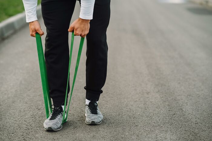 Person exercising with a green resistance band on an outdoor road, demonstrating healthcare workers' fitness routine.