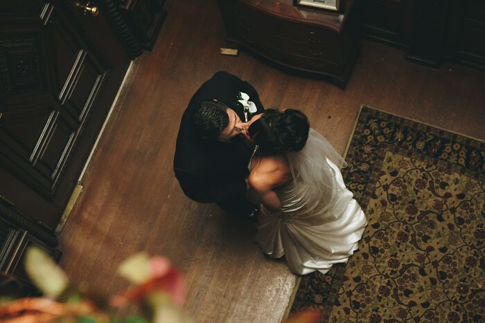 Overhead view of bride and groom kissing on wooden floor near patterned rug in a classic wedding setting for trashy wedding stories.