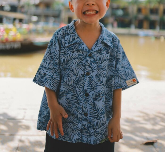Smiling young child wearing a blue patterned shirt outdoors near a waterfront, capturing parenting tips and tricks.