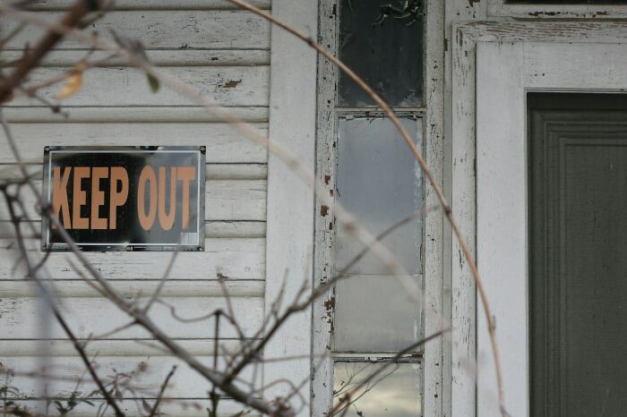 Old weathered house exterior with keep out sign, illustrating karma in all forms and satisfying consequences.