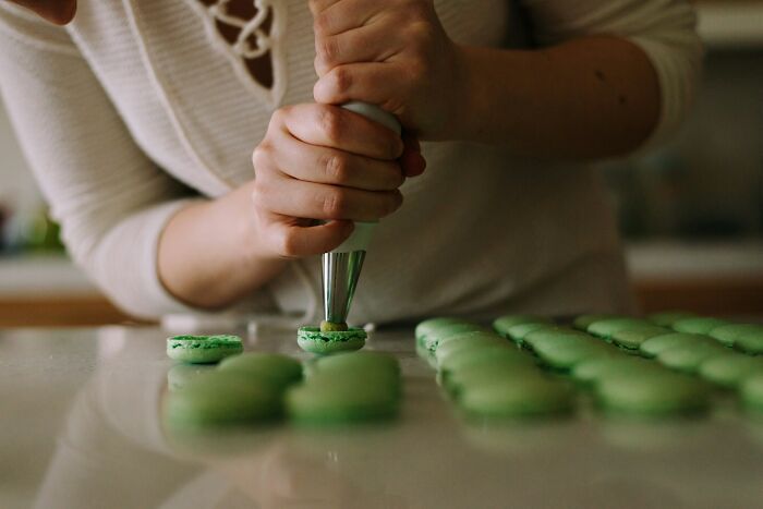 Hands piping filling onto green macarons, illustrating creative jobs AI can’t replace like artisan baking and craftsmanship.