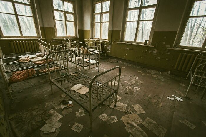 Abandoned room with rusted metal beds and scattered papers, evoking eerie urban legends that were unexpectedly true.