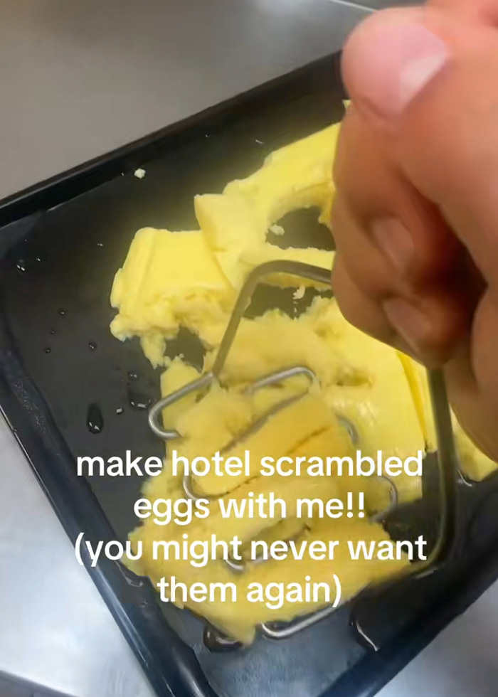 Uma mão usa um espremedor de batatas em uma frigideira com ovos mexidos amarelos. O texto diz, 