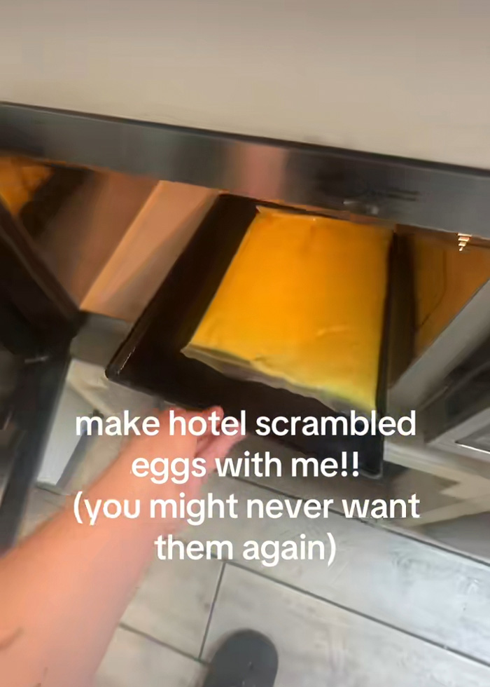 Uma pessoa puxando uma bandeja de ovos do bufê de hotel, envolta em um grande saco plástico, de um aquecedor.