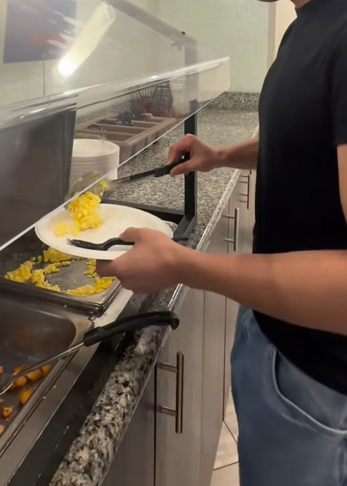 Uma pessoa serve ovos mexidos no buffet de um hotel. Esta imagem está relacionada à forma como os ovos buffet são feitos.