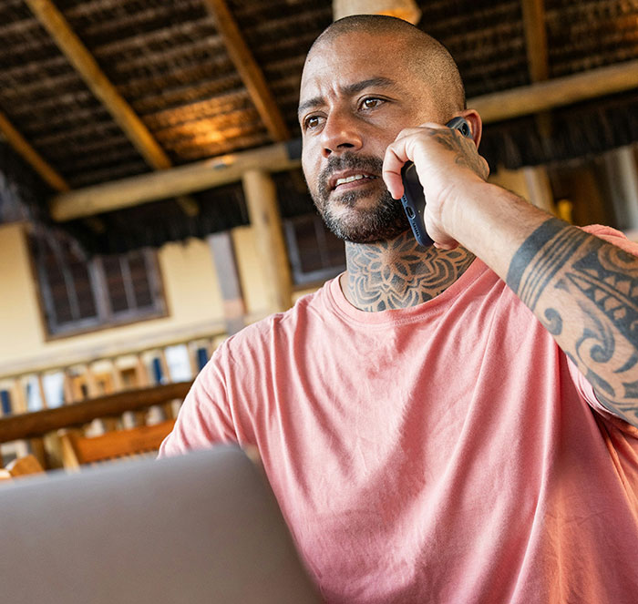 Man with tattoos talking on phone in a hotel setting using a laptop, illustrating tips for an elevated and stress-free stay.