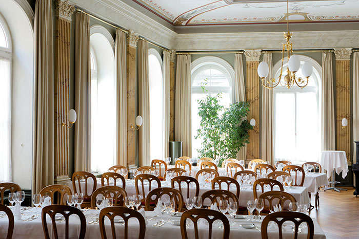 Elegant hotel dining room with wooden chairs and white tablecloths, showcasing tips for an elevated and stress-free hotel stay.