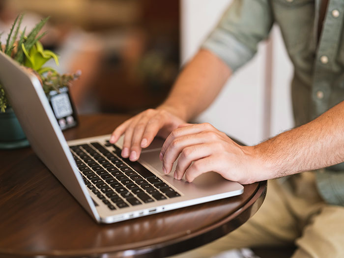 Person typing on a laptop at a wooden table with a plant nearby, focusing on tips for an elevated and stress-free hotel stay