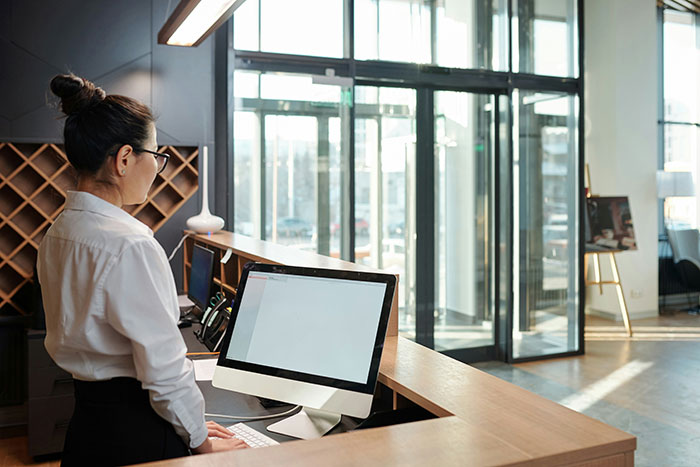 Hotel receptionist at front desk using computer in a modern lobby enhancing a stress-free hotel stay experience